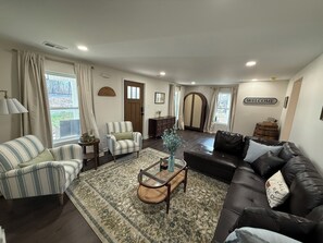 A living room with a striped sofa, a brown leather couch, a striped armchair, a round coffee table, and a large wooden door.