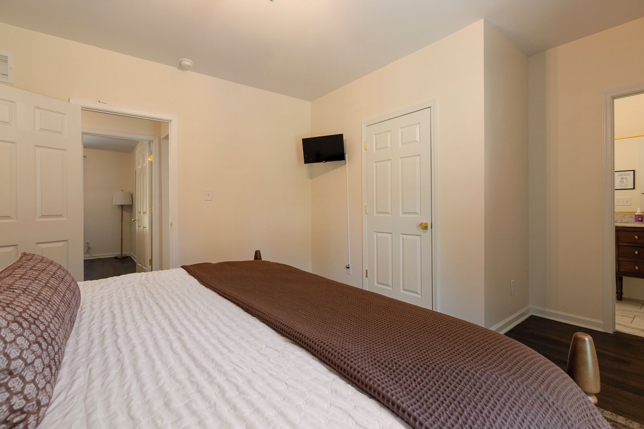 A bedroom with a bed, a television mounted on the wall, and a door leading to another room.