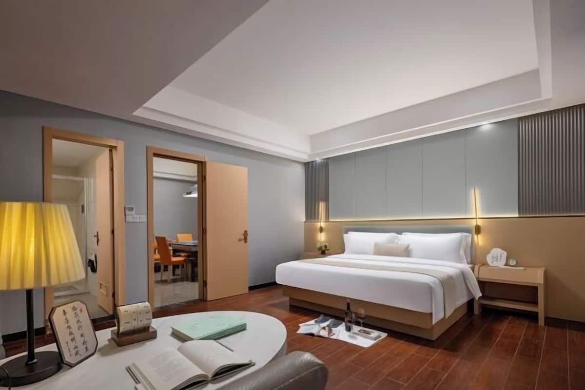 A hotel room with a bed, bedside table, lamp, chair, and a desk with a lamp.