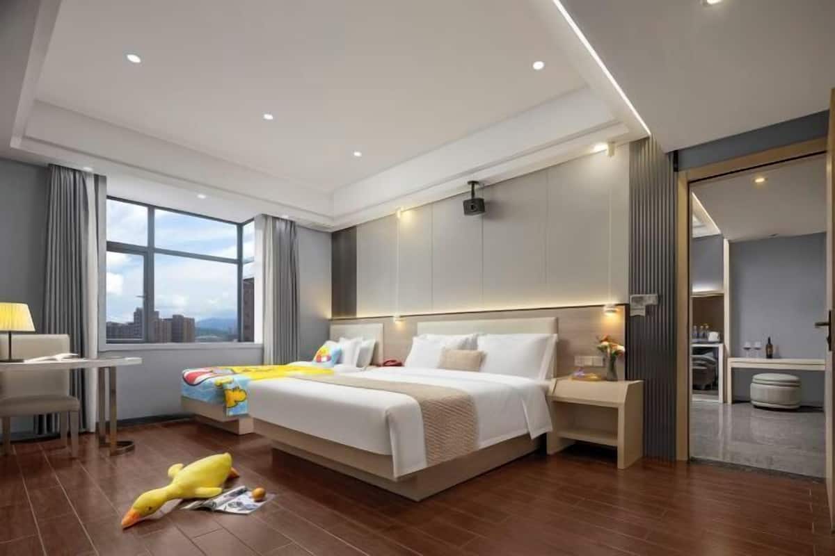 A modern hotel room with a large bed, bedside tables, a desk, and a view of the city.