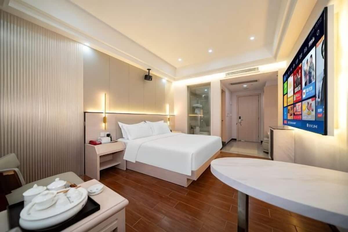 A modern hotel room with a bed, bedside table, and a flat-screen TV mounted on the wall.