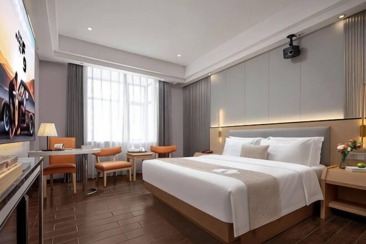A hotel room with a large bed, a desk with a chair, a TV, and a window with curtains.