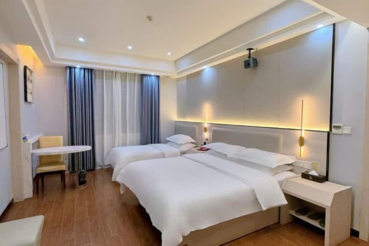 A hotel room with two beds, a small table, a chair, and a large mirror.