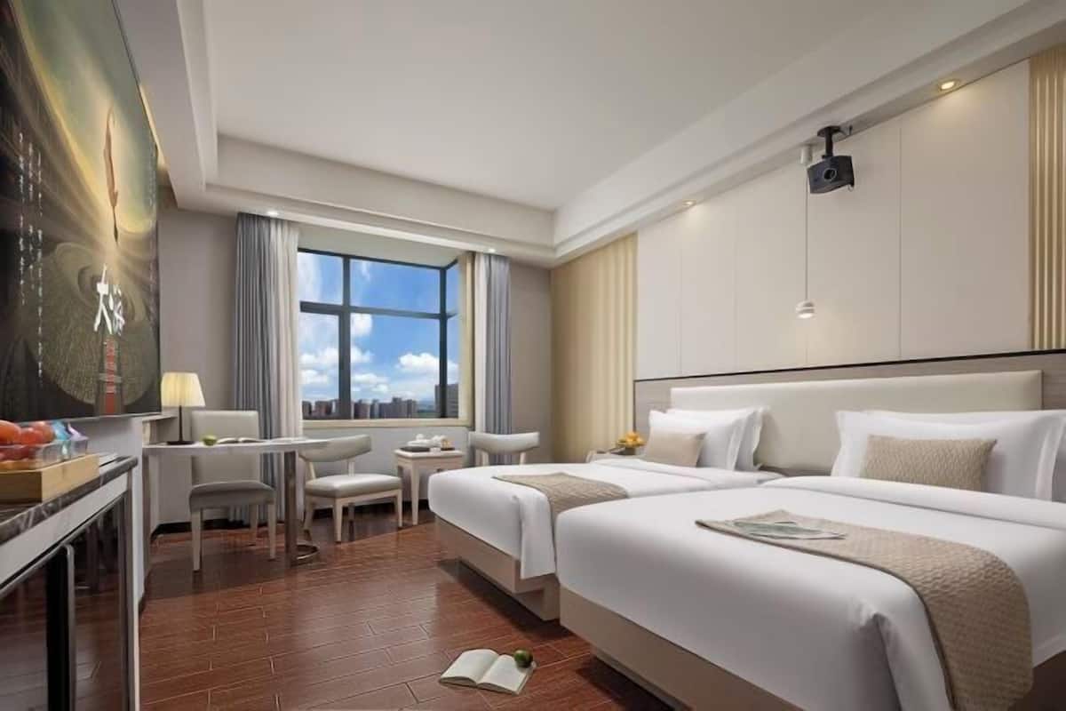 A hotel room with two beds, a desk, a chair, and a large window.