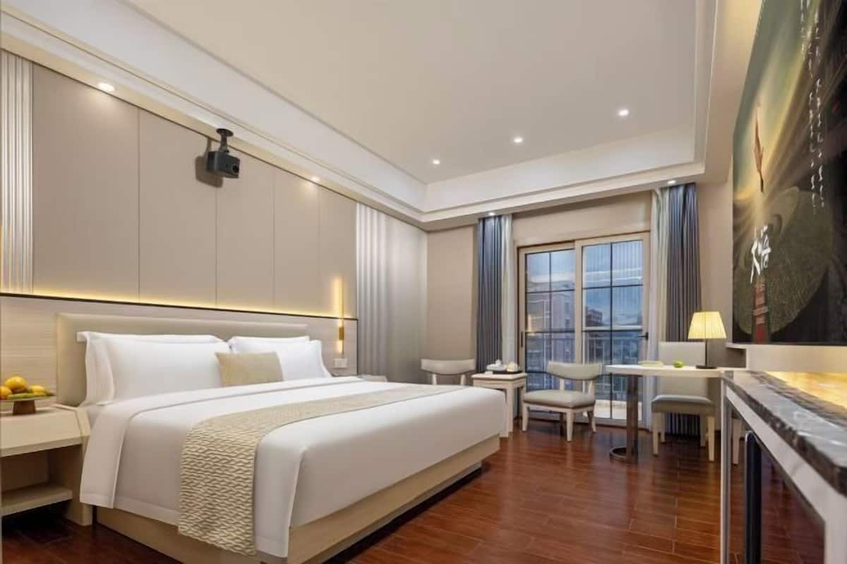 A hotel room with a large bed, a desk, a chair, and a view of the city.