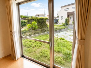 A room with a large sliding glass door leading to a garden area with greenery and a fence.