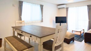 Una sala moderna con una mesa de comedor de madera, sillas blancas, un televisor de pantalla plana y un sofá.