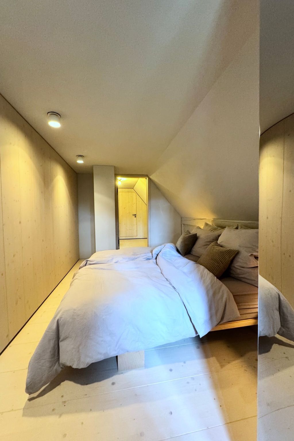 Une chambre avec un plafond en pente, un lit doté d’une tête de lit et un plancher en bois.