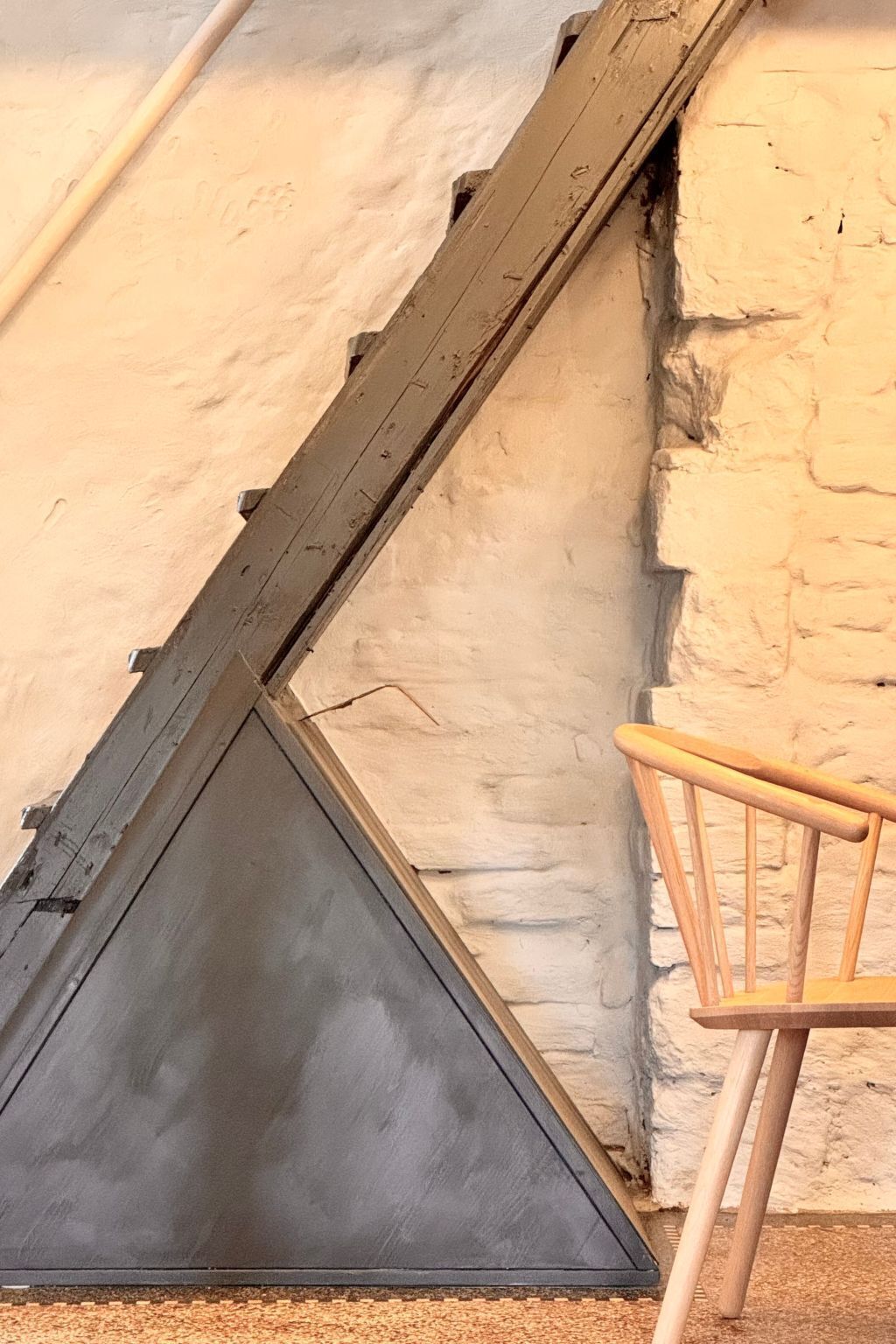 Una habitación con techo inclinado, una silla de madera y una pared con textura.