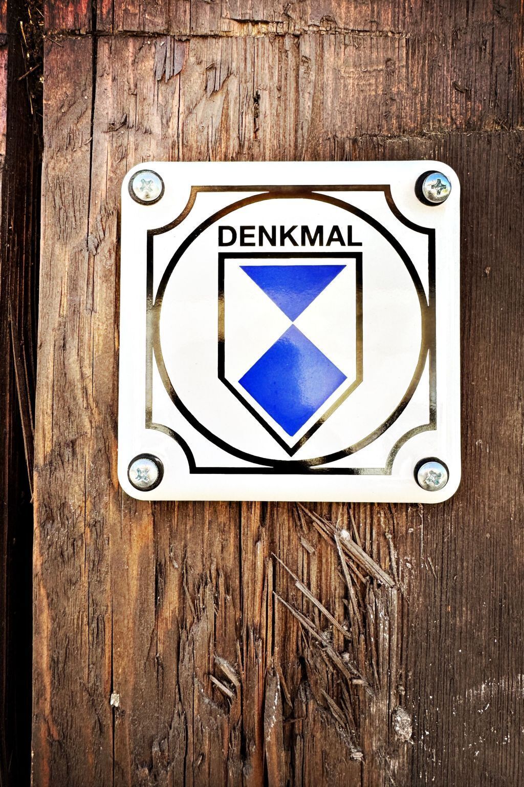 Ein Schild mit dem Wort 'DENKMAL' und einem blau-weißen Wappenschild.