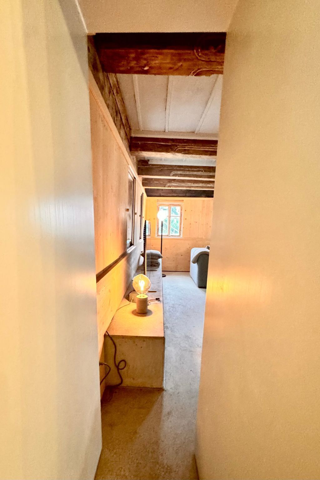 Un pasillo estrecho con techo de madera y un accesorio de luz a la izquierda.