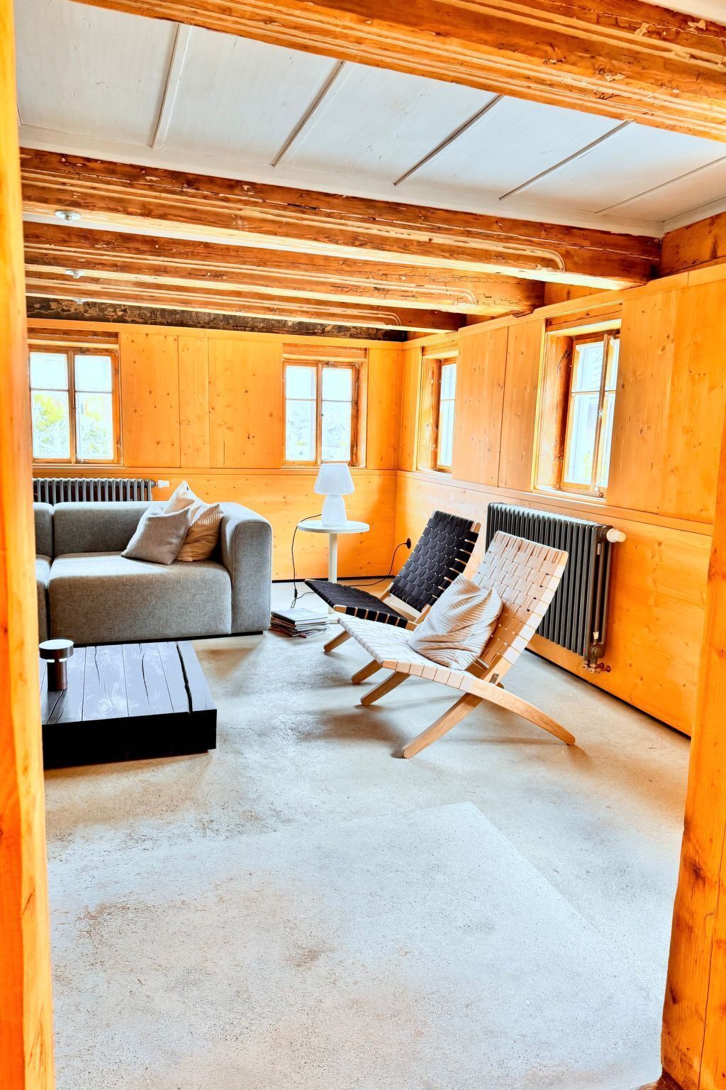 A cozy cabin interior with a sofa, a wooden chair, a small table, and a radiator.