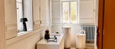 A room with a large window, a radiator, and a white cabinet with a lamp.