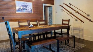 A dining area with a wooden table and chairs, a patterned rug, and skis mounted on the wall. - S'More the Merrier! 3BR/3BA Indian Lake escape. Year round family memories & fun (Indian Lake)