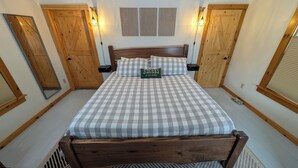 A bedroom with a wooden bed, checkered bedding, a pillow with 'S'mores at dusk, nightly' text, wooden doors, and wall-mounted light fixtures. - S'More the Merrier! 3BR/3BA Indian Lake escape. Year round family memories & fun (Indian Lake)