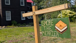 Ein Holzschild mit einer Sandwiches-Illustration und dem Text 'SMORE THE MERRIER'.