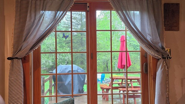 A room with a wooden bench, a patterned rug, and a view of an outdoor deck with a picnic table and umbrella. - S'More the Merrier! 3BR/3BA Indian Lake escape. Year round family memories & fun (Indian Lake)