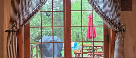 A room with a wooden bench, a patterned rug, and a view of an outdoor deck with a picnic table and umbrella.