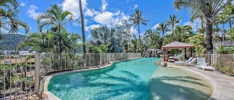 A clear blue pool surrounded by palm trees and a gazebo.