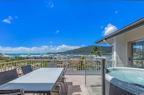A balcony with a table and chairs, a hot tub, and a view of the sea and buildings. - Spa Haven 18A Top Floor Private Spa (Airlie Beach)