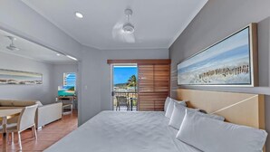 A modern hotel room with a large bed, a dining area, and a balcony with a view. - Spa Haven 18B Top Floor In Room Spa (Airlie Beach)