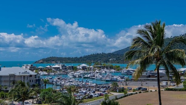 A marina with numerous boats docked, surrounded by buildings and palm trees. - Spa Haven 18B Top Floor In Room Spa (Airlie Beach)