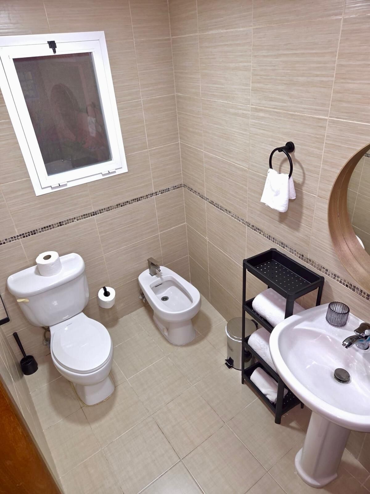A bathroom with two toilets, a bidet, a sink, a mirror, and a towel rack.