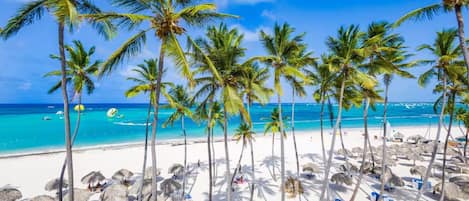 A beach with palm trees and thatched umbrellas.