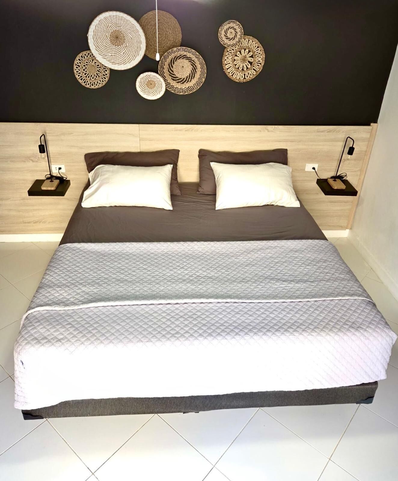 A bed with a quilted cover, two pillows, and a headboard with wall-mounted lights.