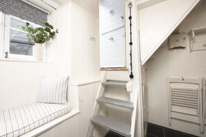 Una escalera estrecha con una puerta blanca y un ventanal pequeño con una planta.