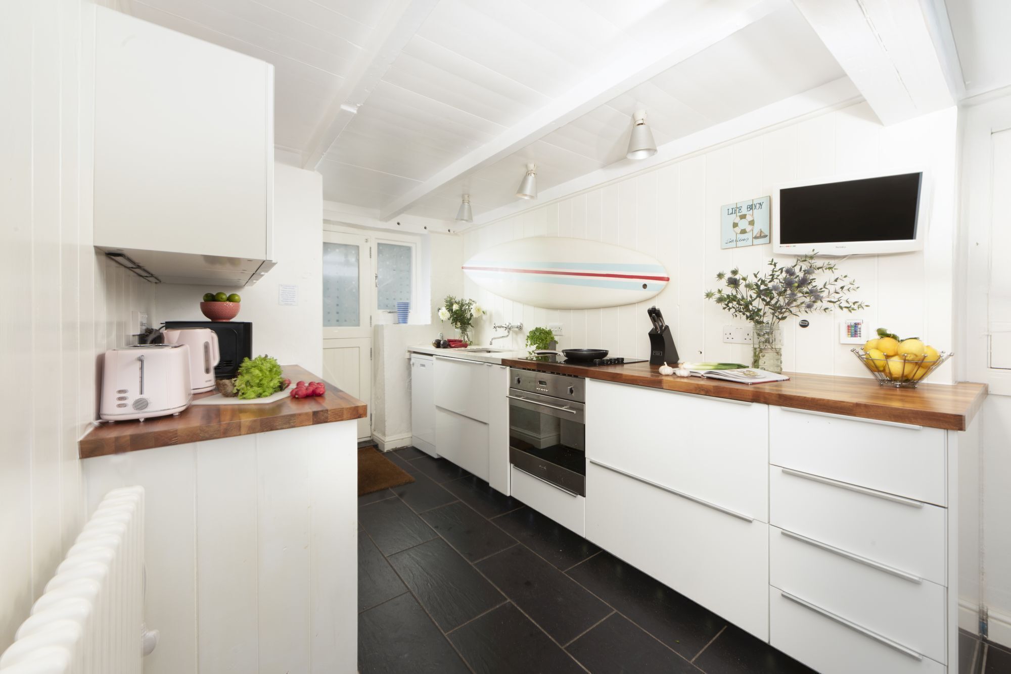 A modern kitchen with white cabinetry, a wooden countertop, a built-in oven, and a large island with a sink and a decorative surfboard.
