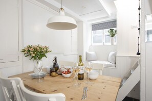Un coin repas avec une table en bois dressée pour le repas, des chaises blanches, une suspension et une fenêtre donnant sur l’ext érieur.
