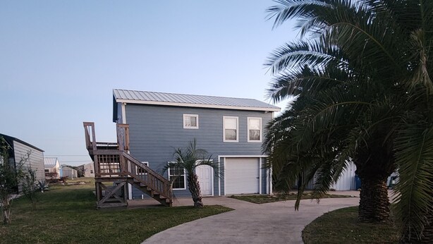Zona residencial con un sendero de hormigón que conduce a una casa de dos plantas con fachada azul.