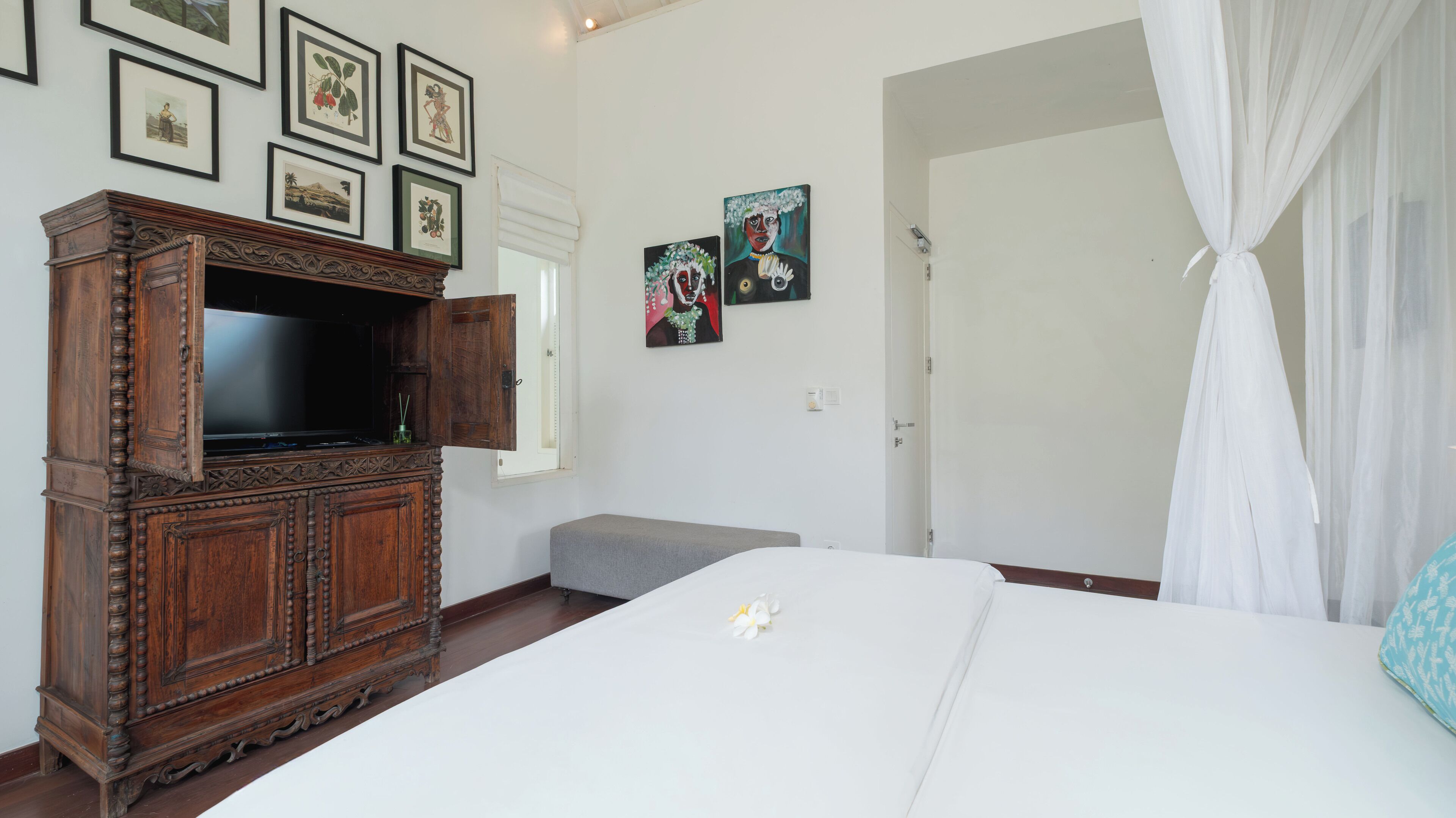 A bedroom with a large bed, a wooden cabinet with a TV, and artwork on the walls.