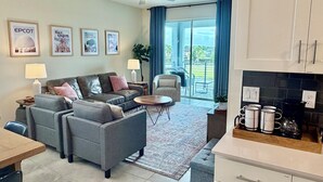 Ein modernes Wohnzimmer mit einer Couch, Sesseln, einem Couchtisch und einem Essbereich mit Tisch und Stühlen. Ein Balkon bietet Blick ins Freie.