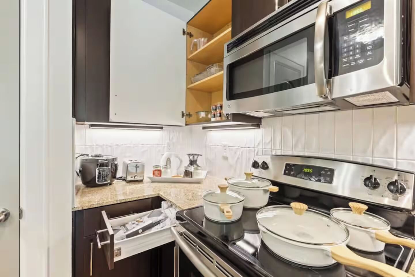A compact kitchen with a microwave, stove, and various cooking pots.