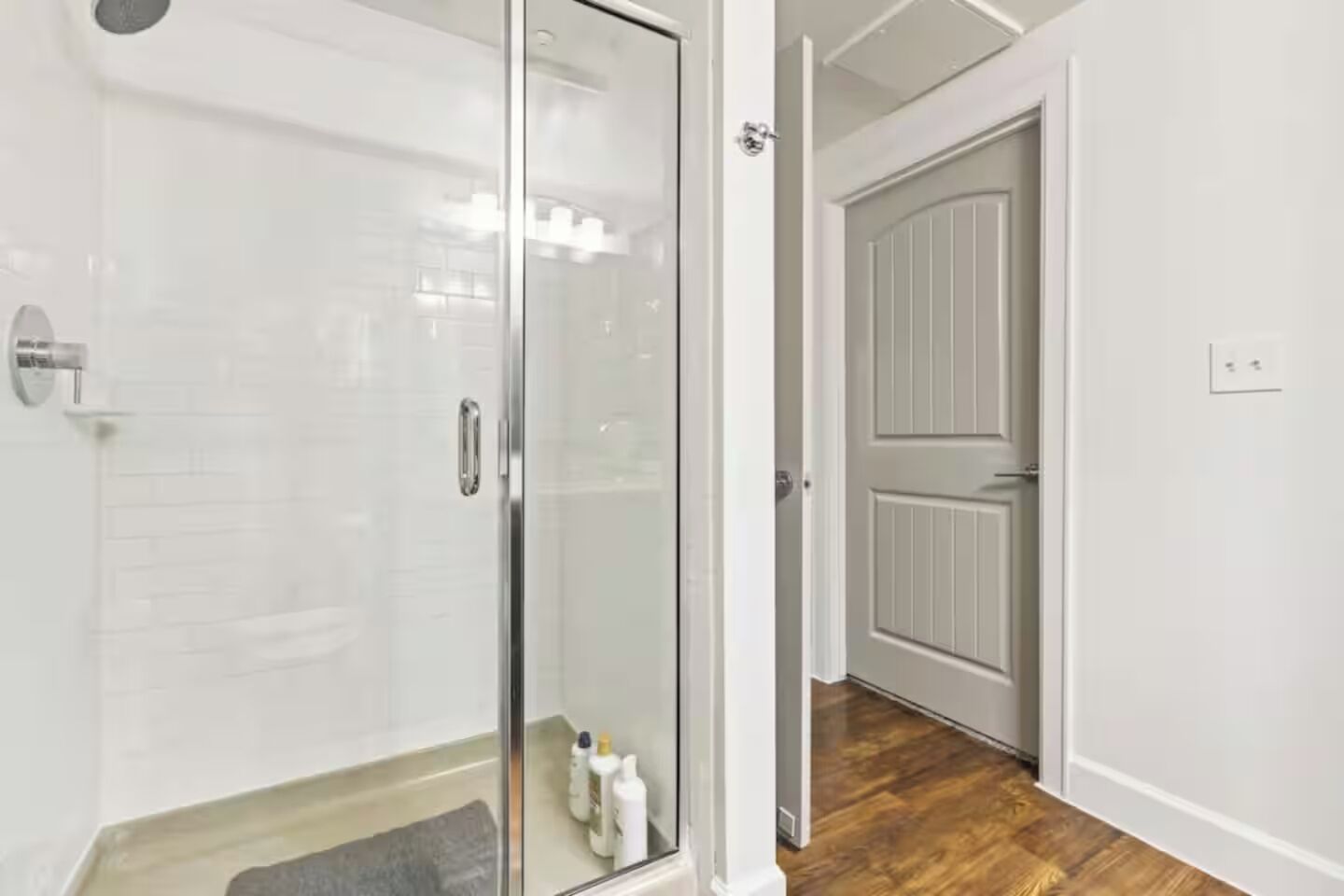 Un baño moderno con cabina de ducha de vidrio, suelo de madera y puerta que da a otra habitación.