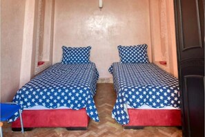 Ein Zimmer mit zwei Betten, jedes mit einer sternenmusternden Tagesdecke und roten Fußhocker.