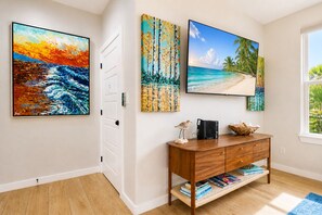Ein Zimmer mit einem Holzkonsolentisch, einem Flachbildfernseher und drei Bildern mit tropischen Motiven.