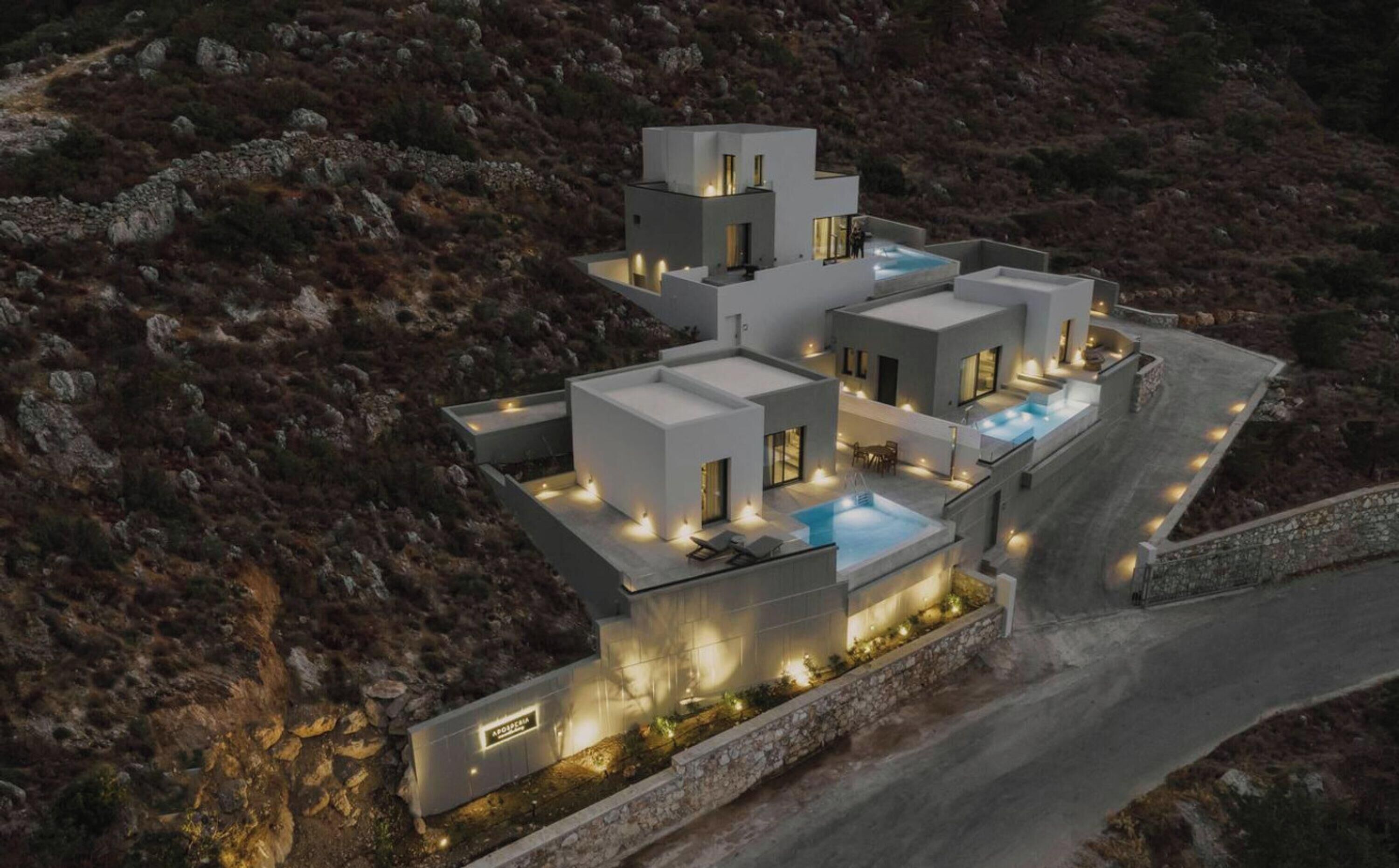 A modern, multi-story house with a rooftop pool, surrounded by rocky terrain.