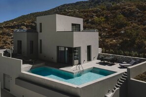 A modern two-story house with a swimming pool, outdoor seating, and a view of a hilly landscape. - Aposperia Memorable Living K3 (Karpathos)