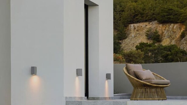 Uma área de piscina moderna com degraus que levam a uma espreguiçadeira, um edifício branco e um cenário de encosta natural.