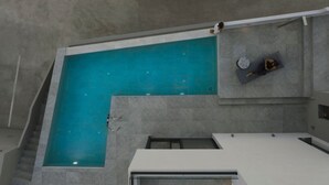 En modern inomhuspool med ett vackert, klart blått vattenparti, en sittgrupp med ett runt bord och en trappa som leder till en annan våning.