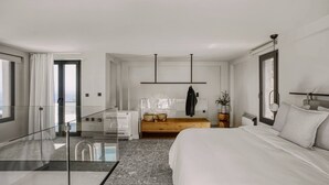 Ett modernt hotellrum med en glasvägg, en träbänk, en säng och utsikt över staden.