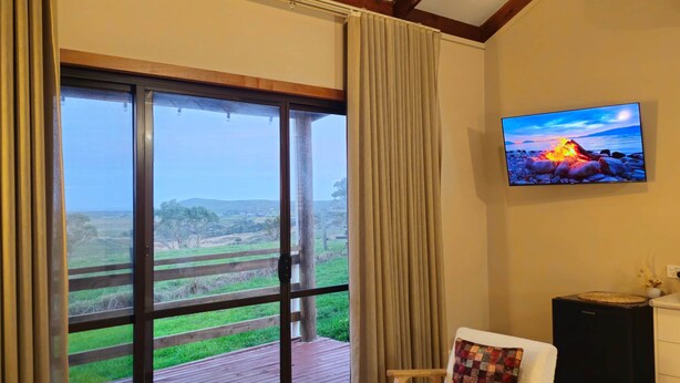 A room with a large sliding glass door leading to a deck, a flat-screen TV mounted on the wall, and a cozy seating area with a sofa and armchairs. - Woop Woop (Princetown)