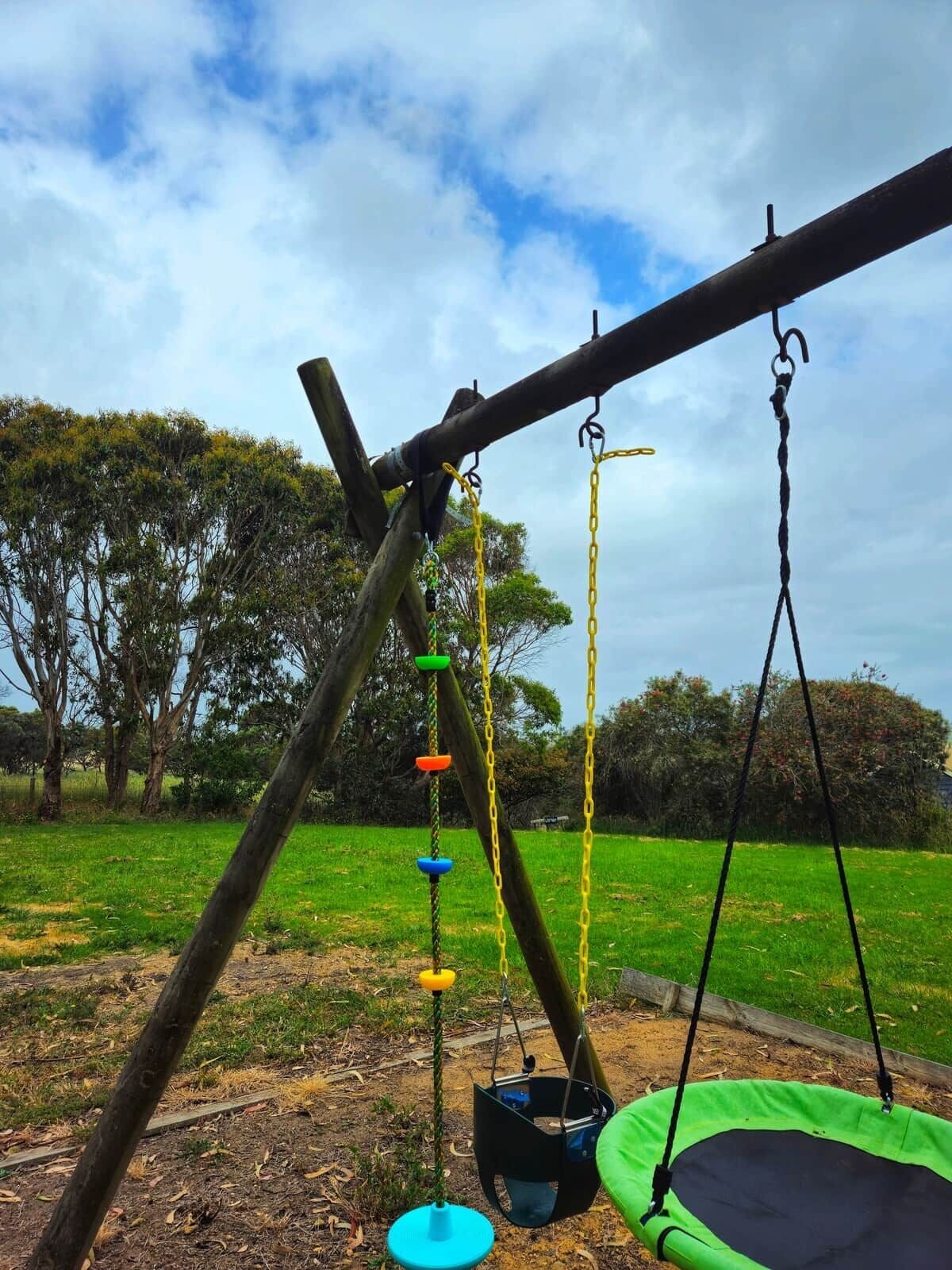 A swing set with a green trampoline and a climbing structure with colorful rings.