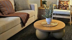 A living room with a sofa, armchair, round coffee table, and a wall-mounted artwork. - Woop Woop (Princetown)