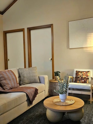 Een woonkamer met een bank, fauteuil, rond salontafeltje en een aan de muur hangend kunstwerk.