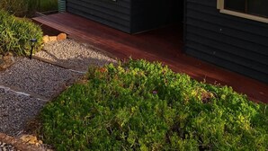 A dark-colored house with a sloped roof, a front porch, and a gravel pathway leading to the entrance. - Woop Woop (Princetown)