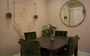 A dining area with a dark wooden table, green upholstered chairs, a vase with flowers, a wall hanging with a geometric pattern, and a round mirror. - Trendy Home +Private Parking+ 5 min walk to Metro (Washington)
